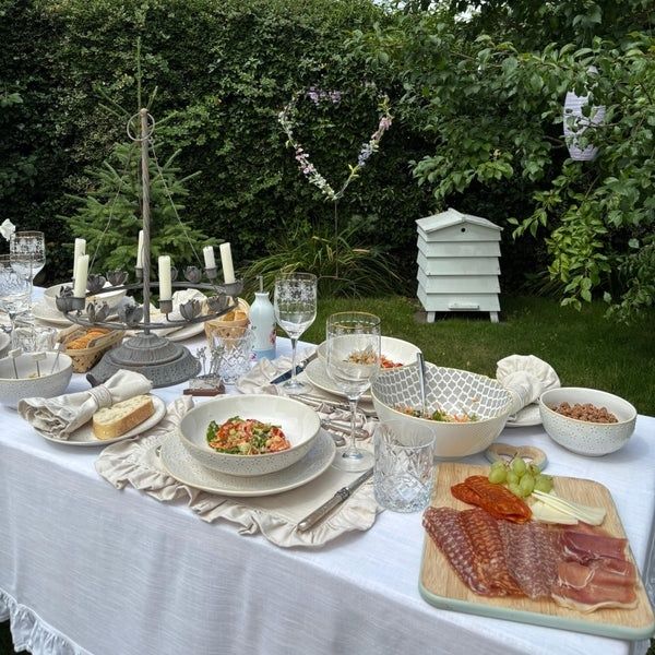 Sommerliche Gartentafel mit Leinen, Keramikgeschirr, Blumen und Wurstplatte