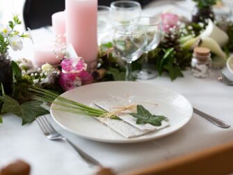 Sommerlich gedeckter Tisch mit Leinenserviette, Wildkräutern und Blumen