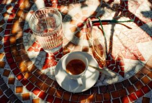 Kaffee, Wasserglas und Sonnenbrille auf einem bunten Mosaiktisch im Freien