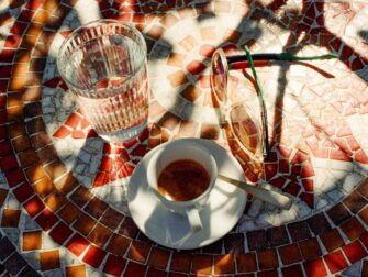 Kaffee, Wasserglas und Sonnenbrille auf einem bunten Mosaiktisch im Freien
