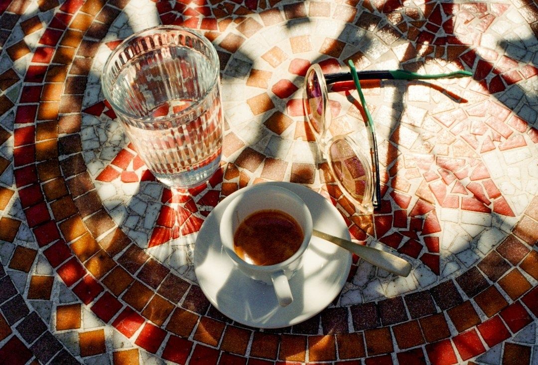 Kaffee, Wasserglas und Sonnenbrille auf einem bunten Mosaiktisch im Freien